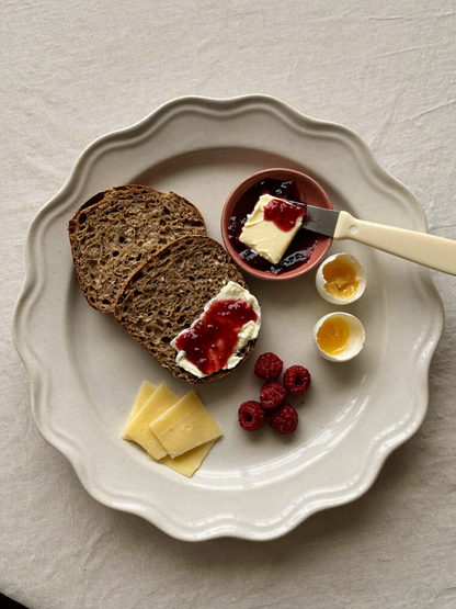 Rugbrød med smør og rød marmelade, serveret med blødkogte æg, osteskiver og friske hindbær på en lys tallerken.